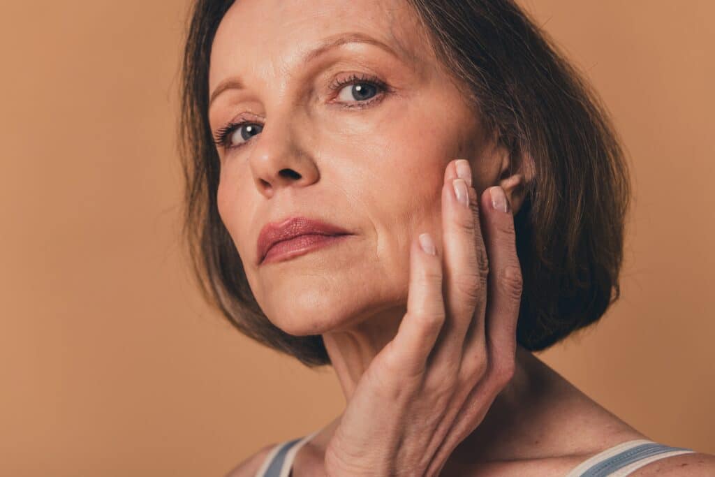 Woman touches her thin face and looks into the camera pensively after losing weight